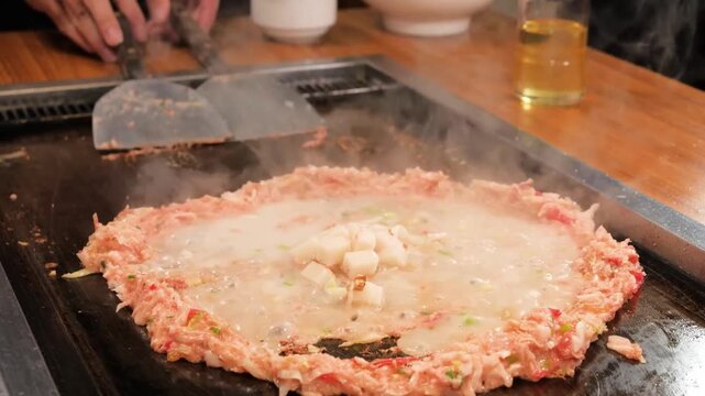 High-quality footage of Monjayaki, a popular Tokyo-style savory pancake, being prepared on a traditional teppanyaki iron griddle. The video shows the iconic "donut" ring of cabbage and ingredients wit
