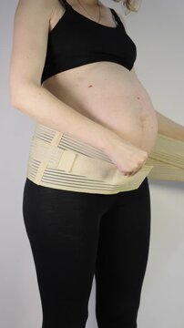 Vertical footage of pregnant woman putting on a supportive maternity belly band for back relief and comfort during pregnancy, close-up.