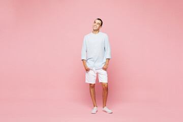 Fototapeta premium Full body smiling happy young middle eastern man he wear casual blue cotton shirt look aside on empty blank area isolated on plain pastel light pink wall background studio portrait. Lifestyle concept.