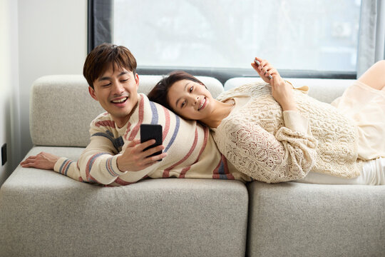 Young couple relax together on the couch, scrolling through their phones
