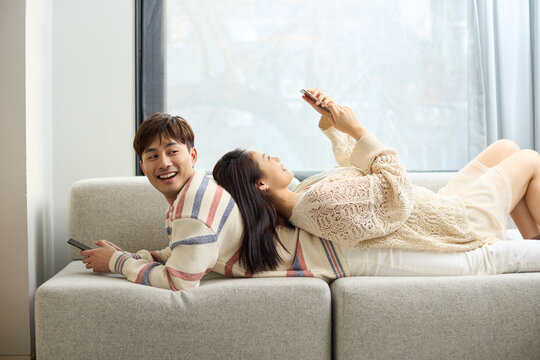 Young couple relax together on the couch, scrolling through their phones