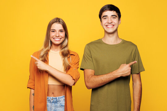 Young smiling happy couple two friends family man woman wear casual clothes point index finger aside on area mock up together isolated on pastel plain light yellow color background studio portrait