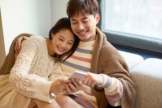 Young couple relax together on the couch, scrolling through their phones
