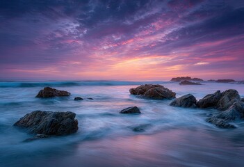 Obraz premium A vibrant sunset paints the sky with hues of pink and purple over a rocky coastline.