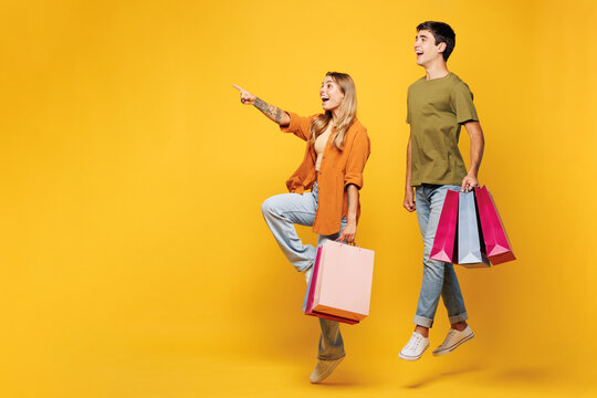 Full body young fun couple two friends family man woman wear casual clothes hold shopping paper package bags point aside together isolated on plain yellow background Black Friday sale buy day concept