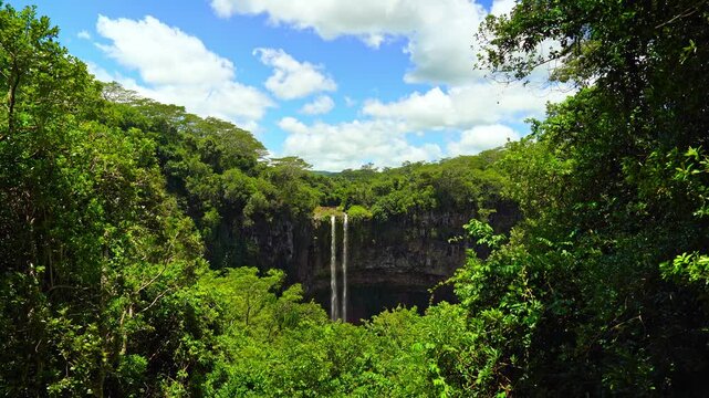 Scenic footage of Chamarel Waterfall in the lush tropical jungle of Mauritius island under a blue sky with white clouds