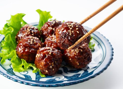 Chopsticks lifting a delicious glazed Japanese meatball with sesame seeds on a white background