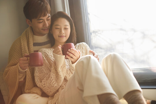 Young couple cuddling under a blanket with hot drinks