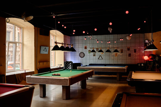 Wide angle shot of billiards club interior featuring multiple pool tables for recreation and social entertainment. Suitable for leisure marketing, nightlife promotion, or venue advertising