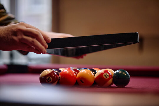 Close up of adult man positioning triangle rack over billiard balls on pool table, preparing game start. Suitable for leisure marketing, bar promotion, recreation content, close up
