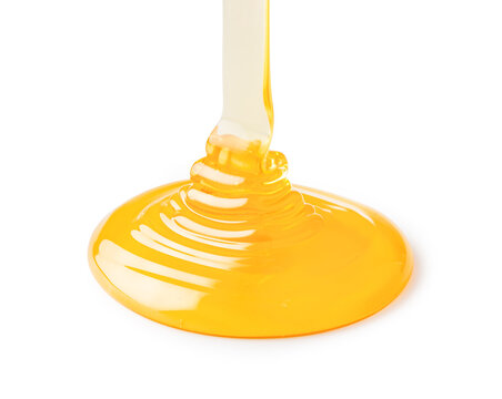 Golden honey pouring creating sweet liquid puddle