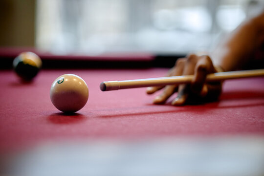 Close up of player aiming cue stick at billiard ball on pool table, showing leisure competition and precision. Suitable for sports marketing, recreation ads, or gaming content
