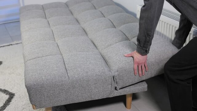 Person folding a grey sofa bed from a sleeping position back into a comfortable sitting sofa in a living room.