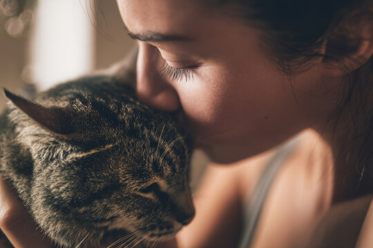 Abstract interpretation of woman gently kissing her cat's head, affectionate pet owner moment, warm indoor lighting mixed with daylight, modern home background softly blurred, emotional connection,