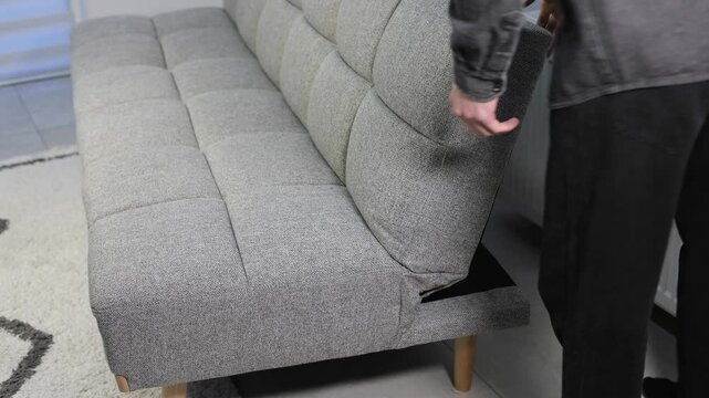 Man transforming a modern grey sofa into a bed, demonstrating functional furniture for small apartment living and comfort.