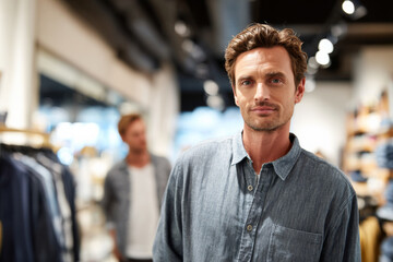 Obraz premium Man looking at camera while standing in clothing store with friend browsing racks behind him, bright retail lighting, modern boutique interior softly blurred, visual for social media concept