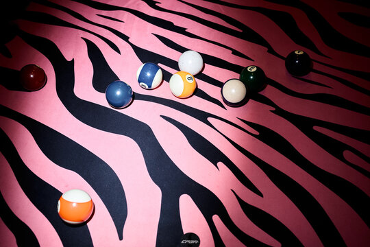 Overhead shot of billiard balls scattering across pink zebra pattern surface, suggesting playful leisure branding and retro entertainment theme. Suitable for nightlife marketing or game venue ads
