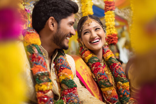Minimal indian bride and groom laughing together while exchanging flower garlands during varmala ceremony, colorful flowers and festive decorations, bright natural daylight isolated on clean