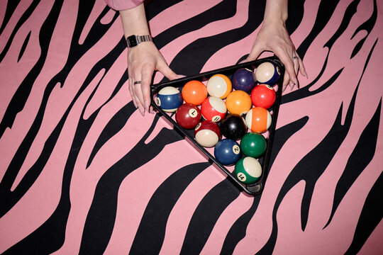 Overhead shot of young adult woman hands arranging billiard balls in rack on patterned table, suggesting leisure gaming and nightlife branding. Useful for entertainment marketing or social event promo