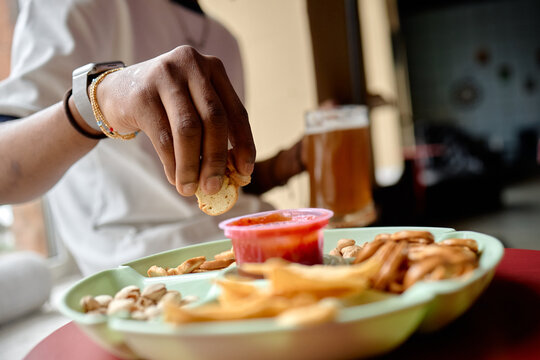 Close up of young adult woman dipping cracker into sauce while snacking with beer at cafe table. Suitable for casual dining, social lifestyle, food service or beverage marketing
