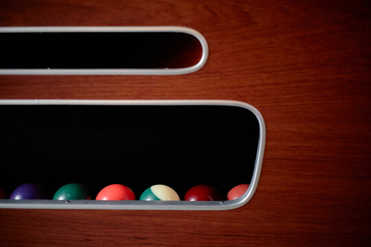 Close up of billiard balls resting inside pool table return slot, illustrating leisure gaming and recreation concept. Suitable for sports bar marketing, entertainment ads, copy space
