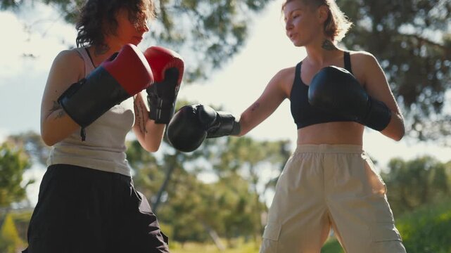 Two women boxers sparring together in a sunny park