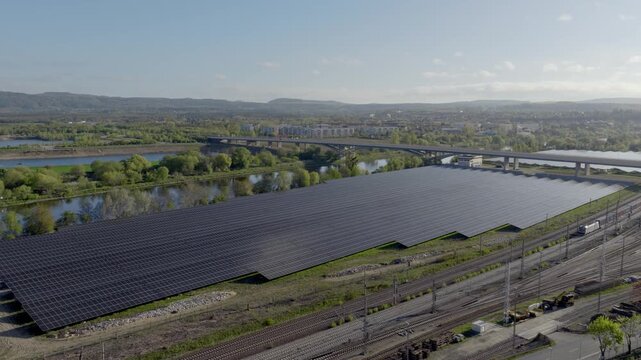Aerial view of a large solar farm next to railway tracks and a highway bridge, symbolizing energy transition and modern infrastructure. with driving trains 