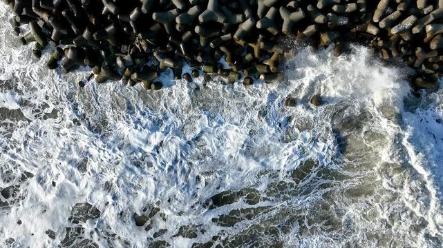 Aerial top-down geometric view of harbor concrete structure with tetrapods and waves, Tomioka