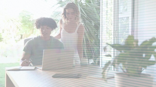 Woman leaning over man at table, leading man typing and gesturing on laptop during design review