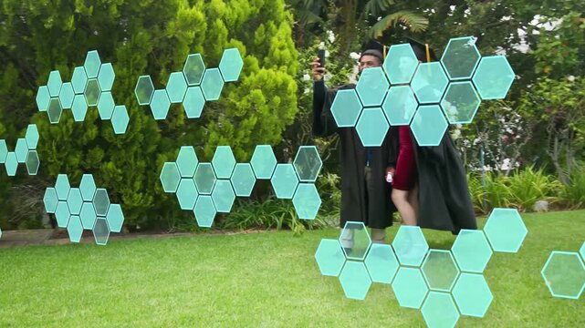 Two grads walking lawn raising phone selfie celebrating diplomas teal hexes floating obscuring view