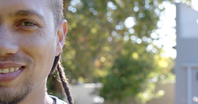 African American man smiling, widening grin, squinting with joy in sunlit yard, dreads, copy space