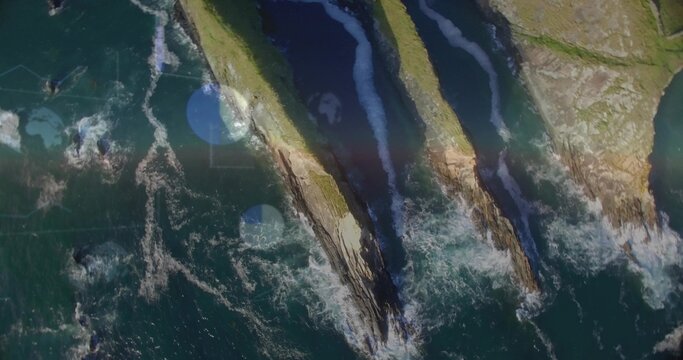 Showing three sea stacks jutting into choppy ocean from above, with grassy tops and lens flares