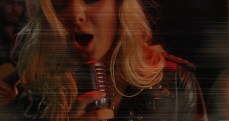 Fototapeta premium Singing female singer holding retro mic on club stage, wearing studded jacket, guitar neck visible