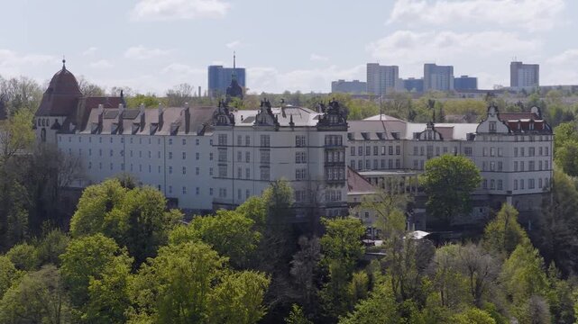 View of the historic Sonnenstein Castle in Pirna against a modern urban backdrop with high-rise buildings under a slightly cloudy sky.