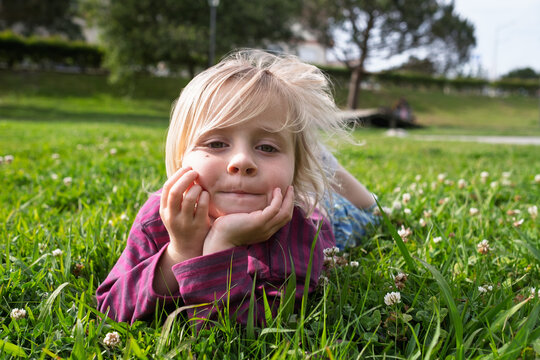 Summer Serenity: Little Girl Relaxing and Dreaming on Green Grass in a City Park