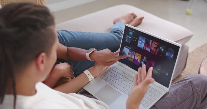 African American couple scanning tiles, pointing, navigating laptop trackpad on couch choosing show