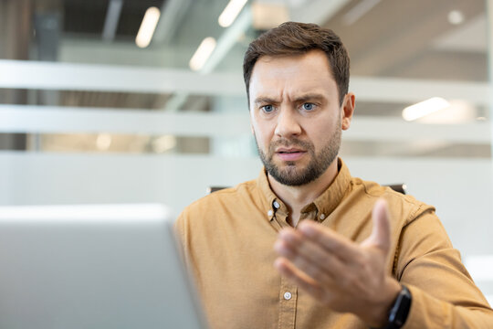 Man experiencing confusion and frustration while working on a laptop, making a questioning gesture, indicating a software error, technical issue, or data problem in a modern office environment