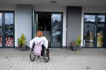 Woman in wheelchair entering modern building with accessible entrance.