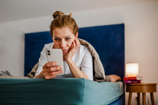 Woman lying under blanket and scrolling on phone.