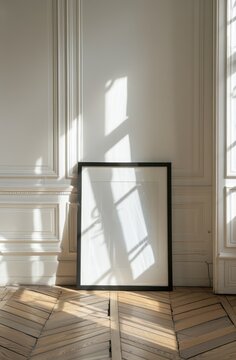 Minimalist blank black poster frame mockup leaning against a white paneled wall with dramatic window shadows on parquet wooden floor, elegant warm sunlight aesthetic for art display.