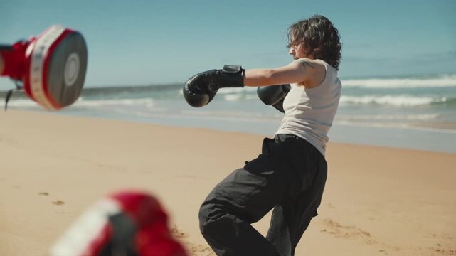 Tattooed woman kickboxing training on a sunny beach