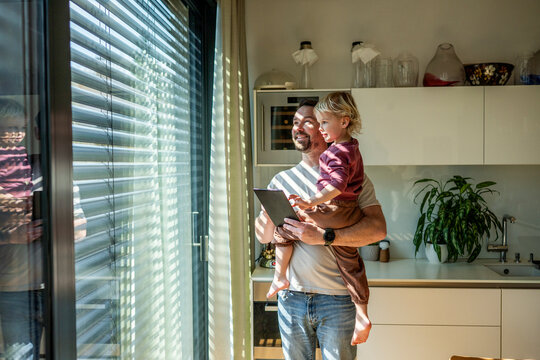 Father showing smart home control to toddler while managing exterior shading system.
