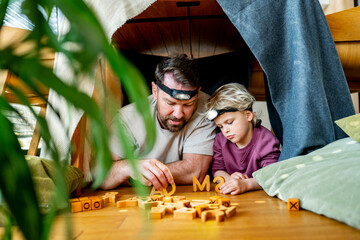 Dad and child building and playing in cozy blanket fort.