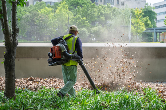 Worker in High-Visibility Vest Using Backpack Leaf Blower in Urban Park