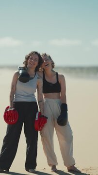 Two female boxers smiling together on a sandy beach