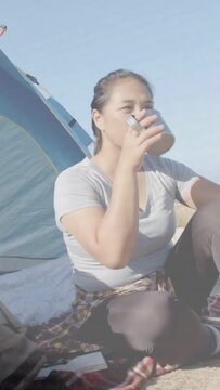 Vertical video: Camper lifting cup and sipping while resting, causing motion icons tagging tent