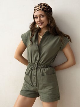 Stylish Young Woman in Casual Olive Green Outfit with Accessories Posing Confidently Against a Neutral Background
