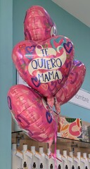 Obraz premium Grupo de globos de color rosa con forma de corazón, con texto en español Te quiero mamá, decorando el interior de una tienda para el Día de la madre 