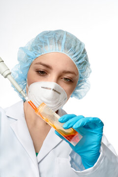 Woman pipetting with micropipette into cell culture flask with orange medium