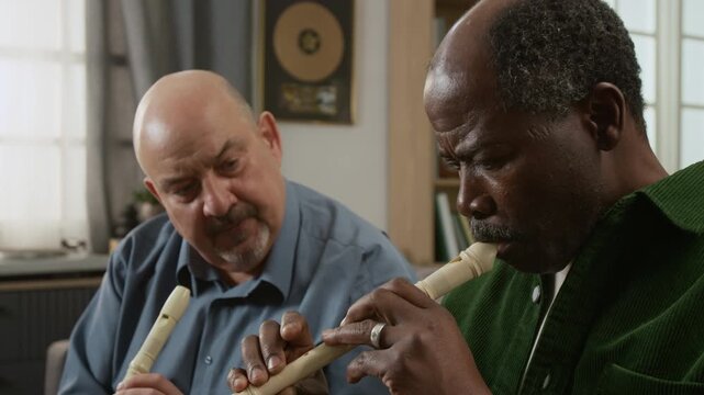 Side view close up shot of middle aged music teacher demonstrating technique and correcting senior African American man learning to play recorder Suitable for educational content